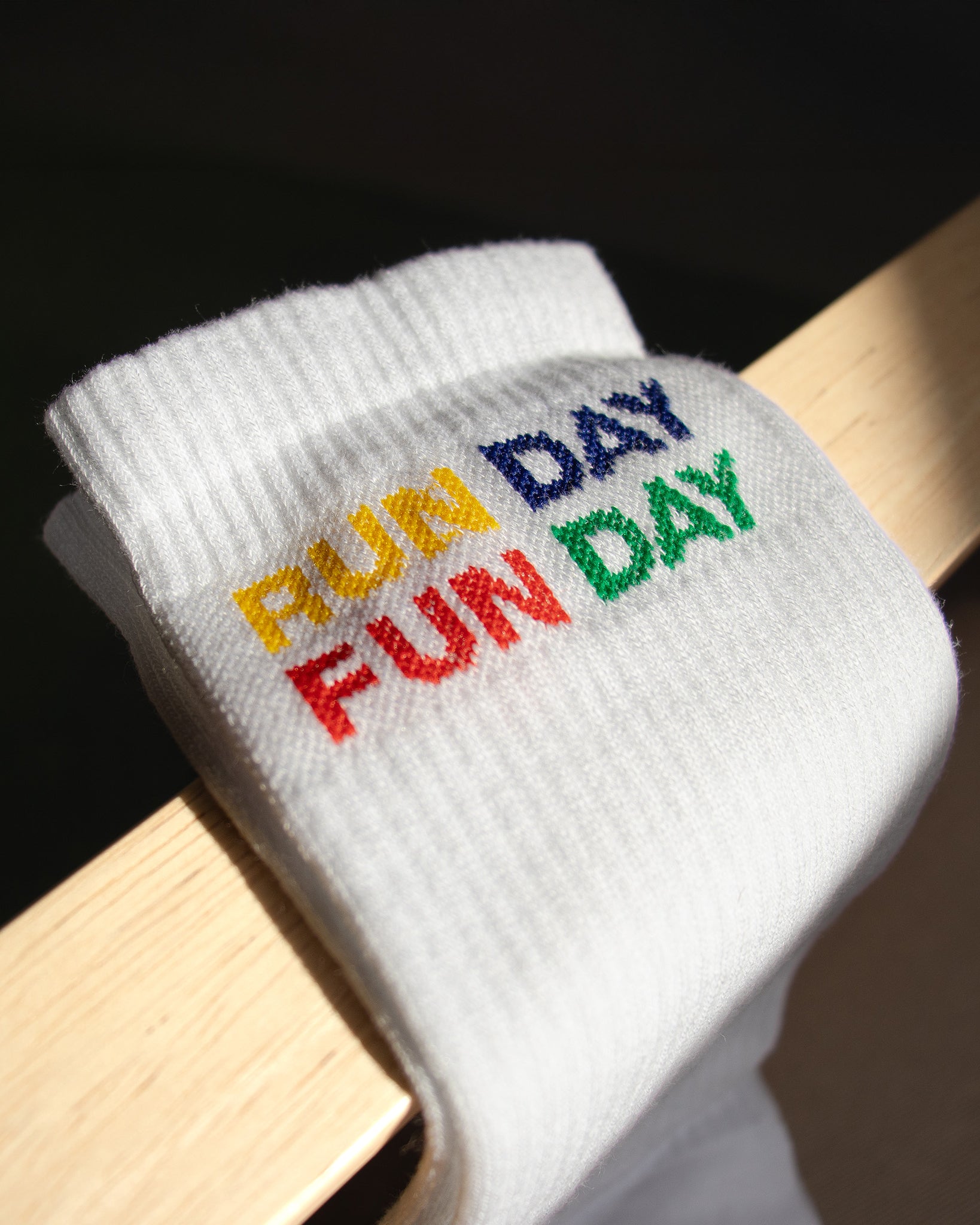 Detalle del bordado multicolor RUN DAY FUN DAY en los calcetines blancos de Färgen bajo luz natural.