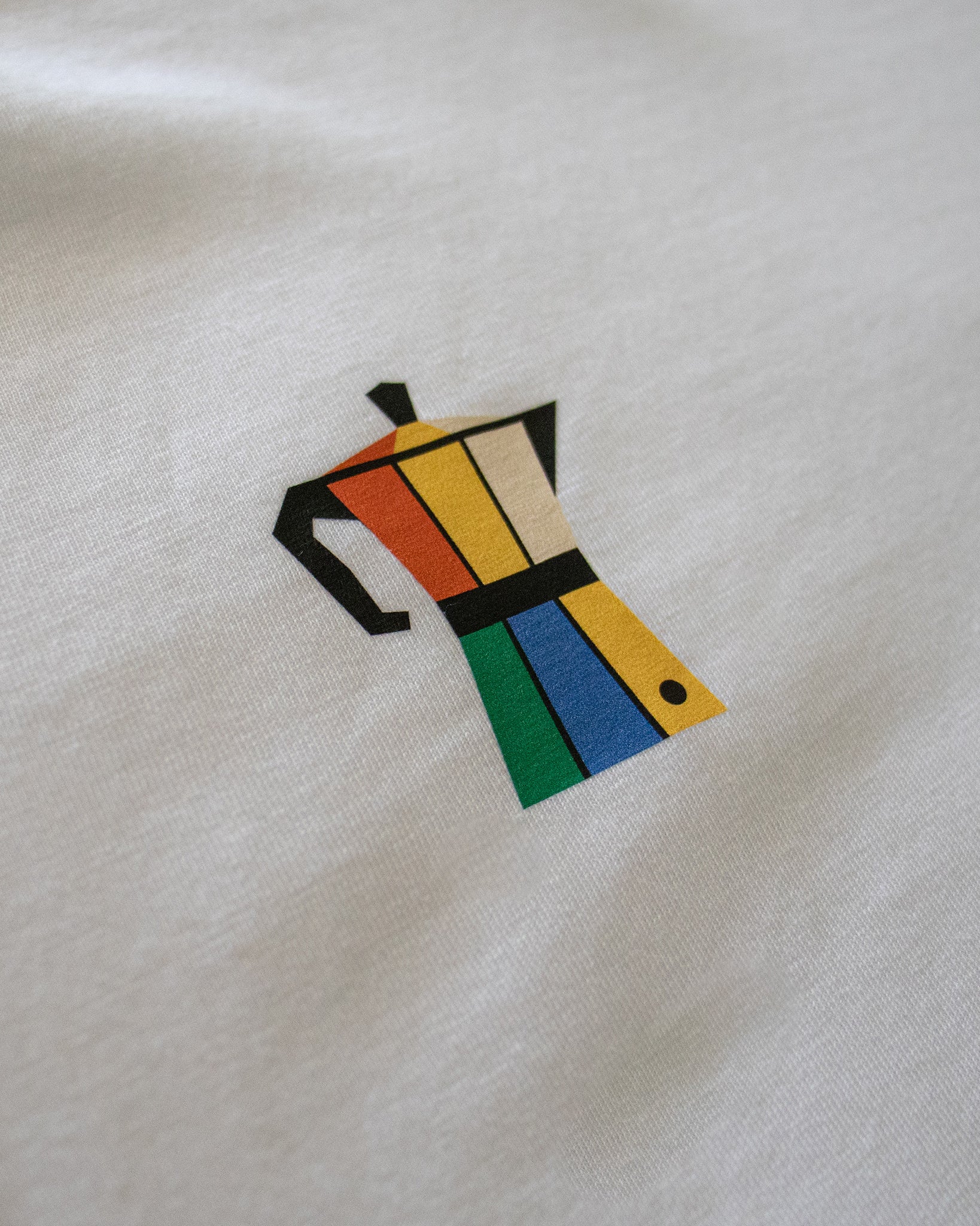 Detalle del diseño de cafetera italiana de colores en el pecho de la camiseta Färgen Il Caffè di Casa. Estilo Bauhaus