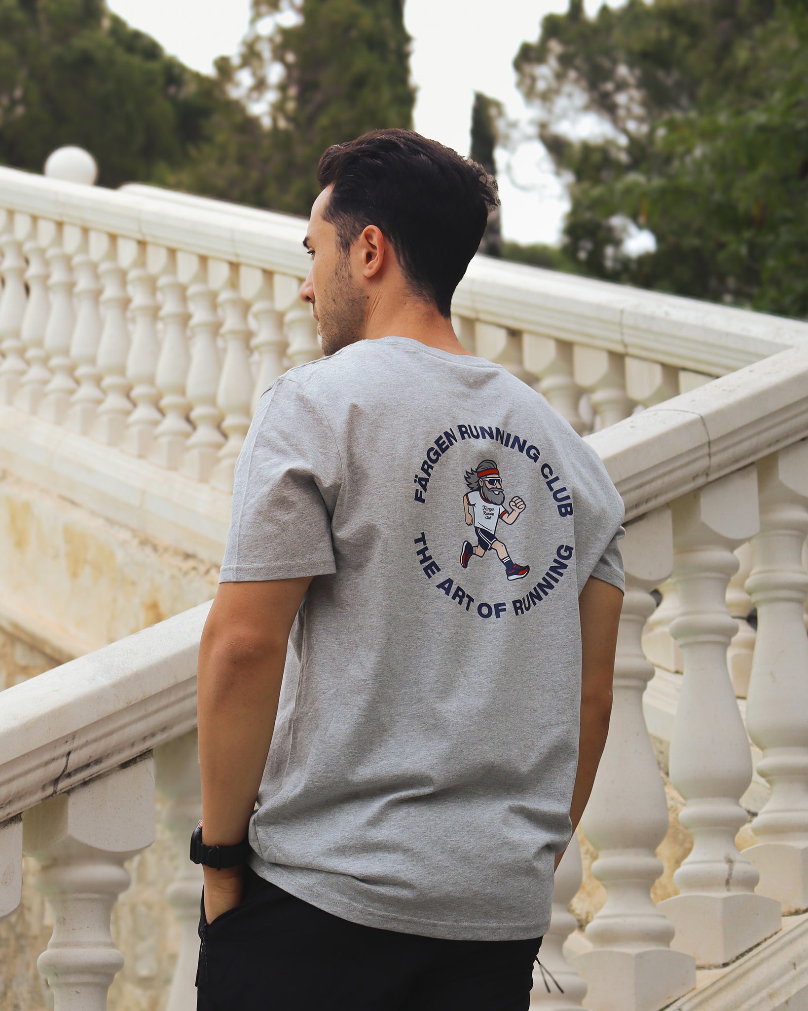 Hombre con camiseta gris Färgen Running Club mostrando el diseño trasero con corredor y texto The Art of Running.