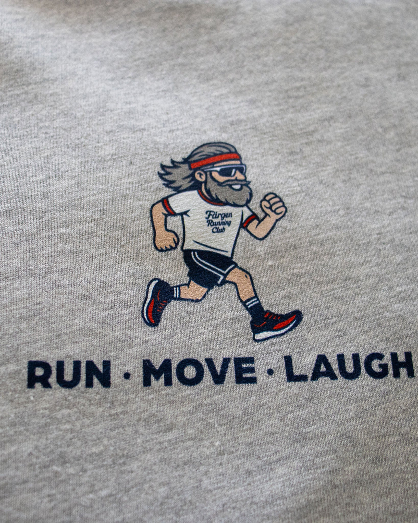 Detalle del estampado del corredor y lema RUN MOVE LAUGH en la camiseta gris Färgen Running Club.