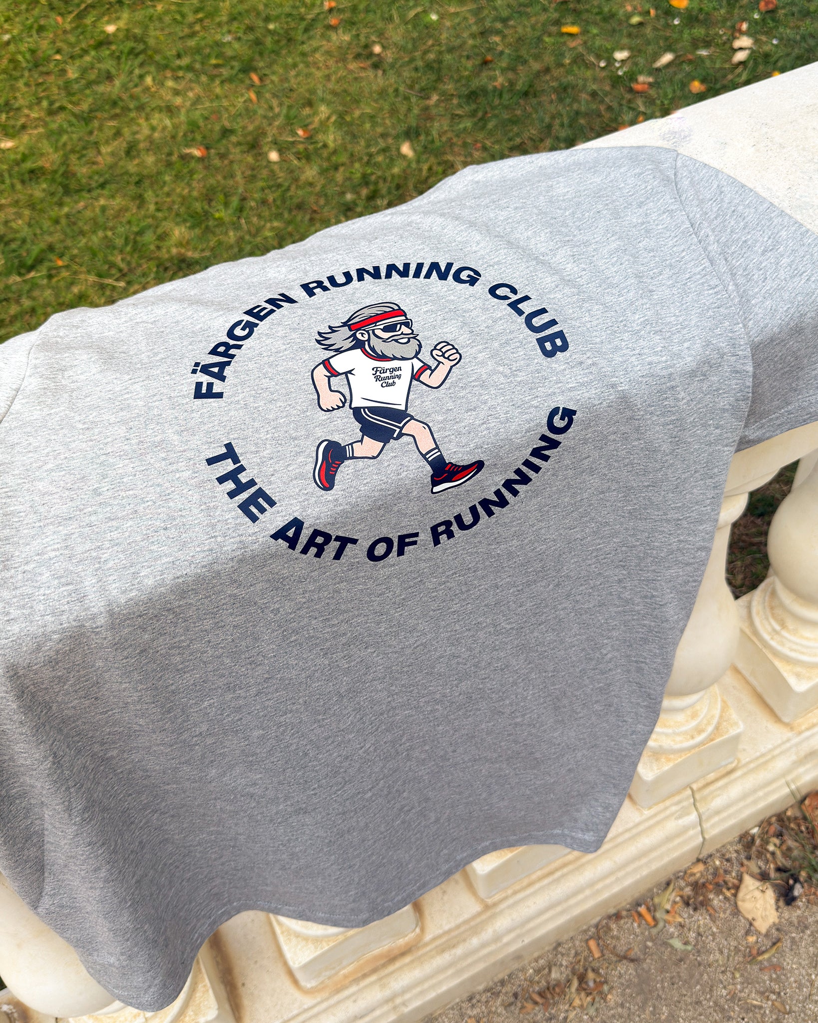 Camiseta gris Färgen Running Club doblada sobre barandilla mostrando el diseño trasero con corredor y texto The Art of Running.
