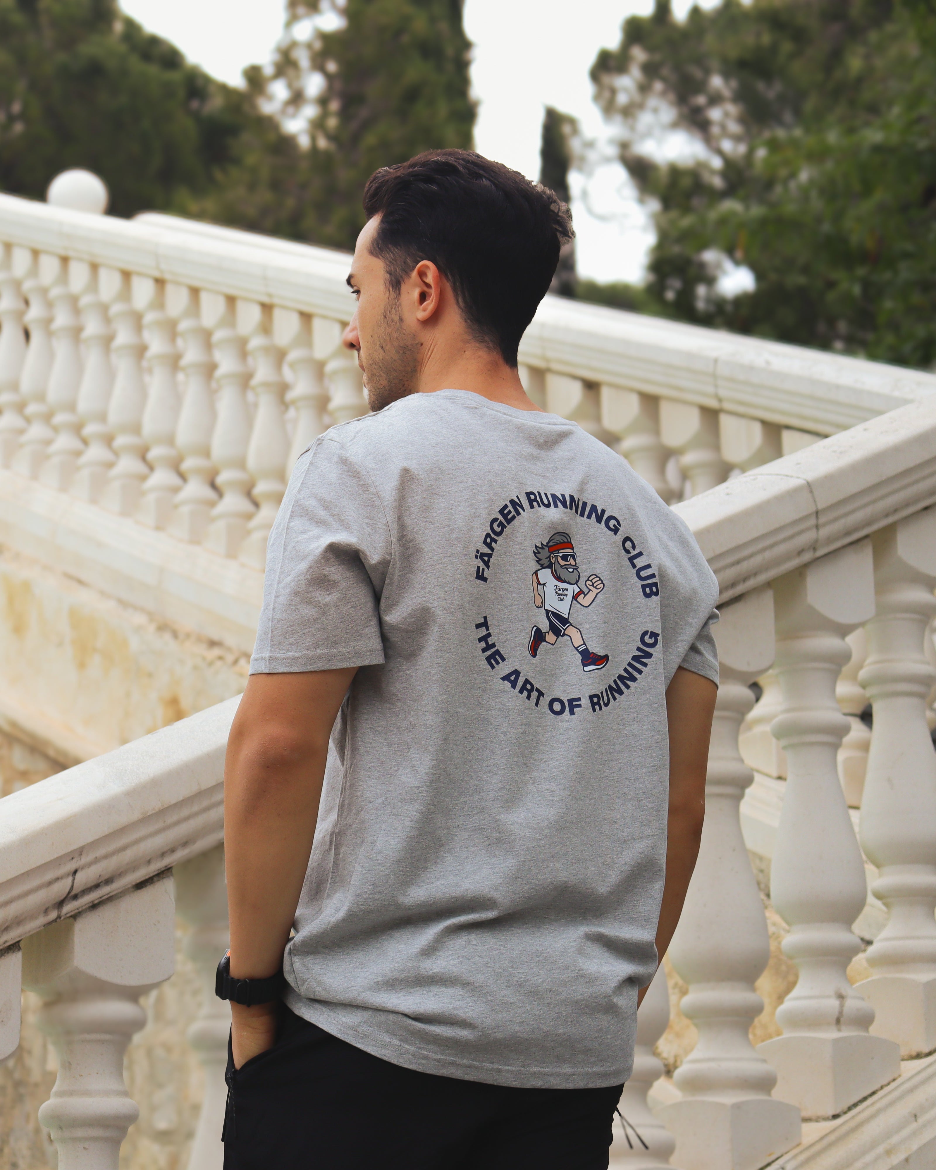 Hombre con camiseta gris Färgen Running Club mostrando el diseño trasero con corredor y texto The Art of Running.