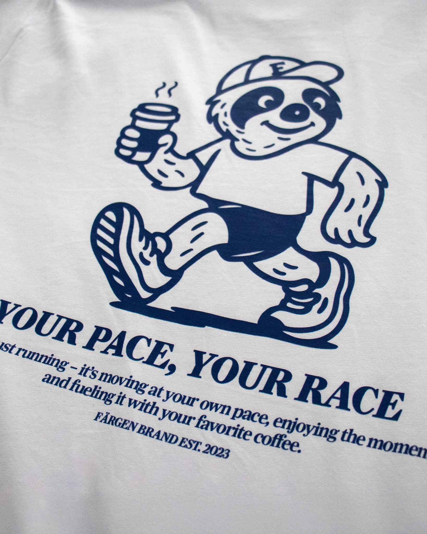 Detalle del diseño trasero de la camiseta Färgen Your Pace Your Race con perezoso corriendo y taza de café.