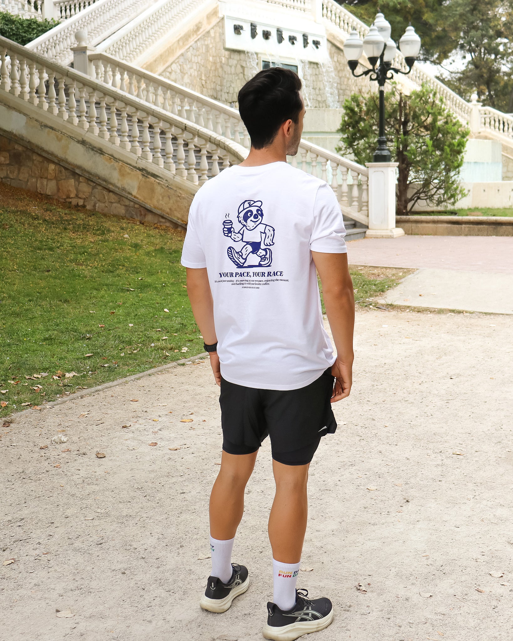 Hombre con camiseta blanca Färgen Your Pace Your Race mostrando el diseño trasero con el perezoso corriendo y el texto en azul.