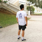Hombre con camiseta blanca Färgen Your Pace Your Race mostrando el diseño trasero con el perezoso corriendo y el texto en azul.