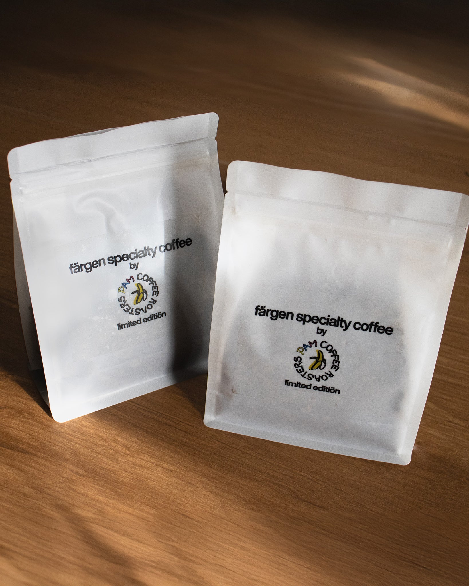 Dos bolsas de café Färgen Specialty Coffee x Pam Coffee Roasters edición limitada, colocadas sobre una superficie de madera.