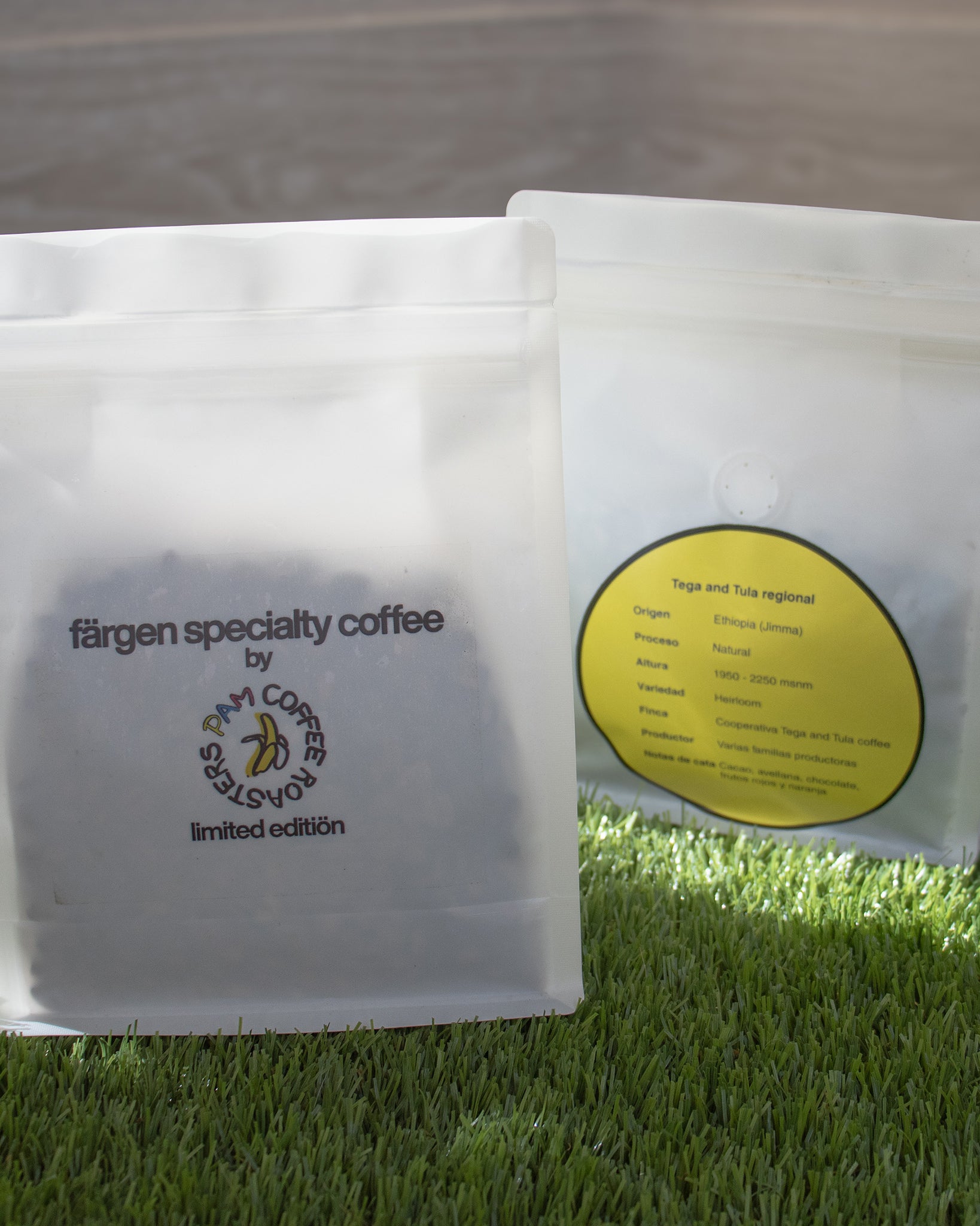 Bolsas del café Färgen Specialty Coffee x Pam Coffee Roasters sobre césped, mostrando el diseño frontal y la etiqueta de origen Etiopía Tega & Tula.