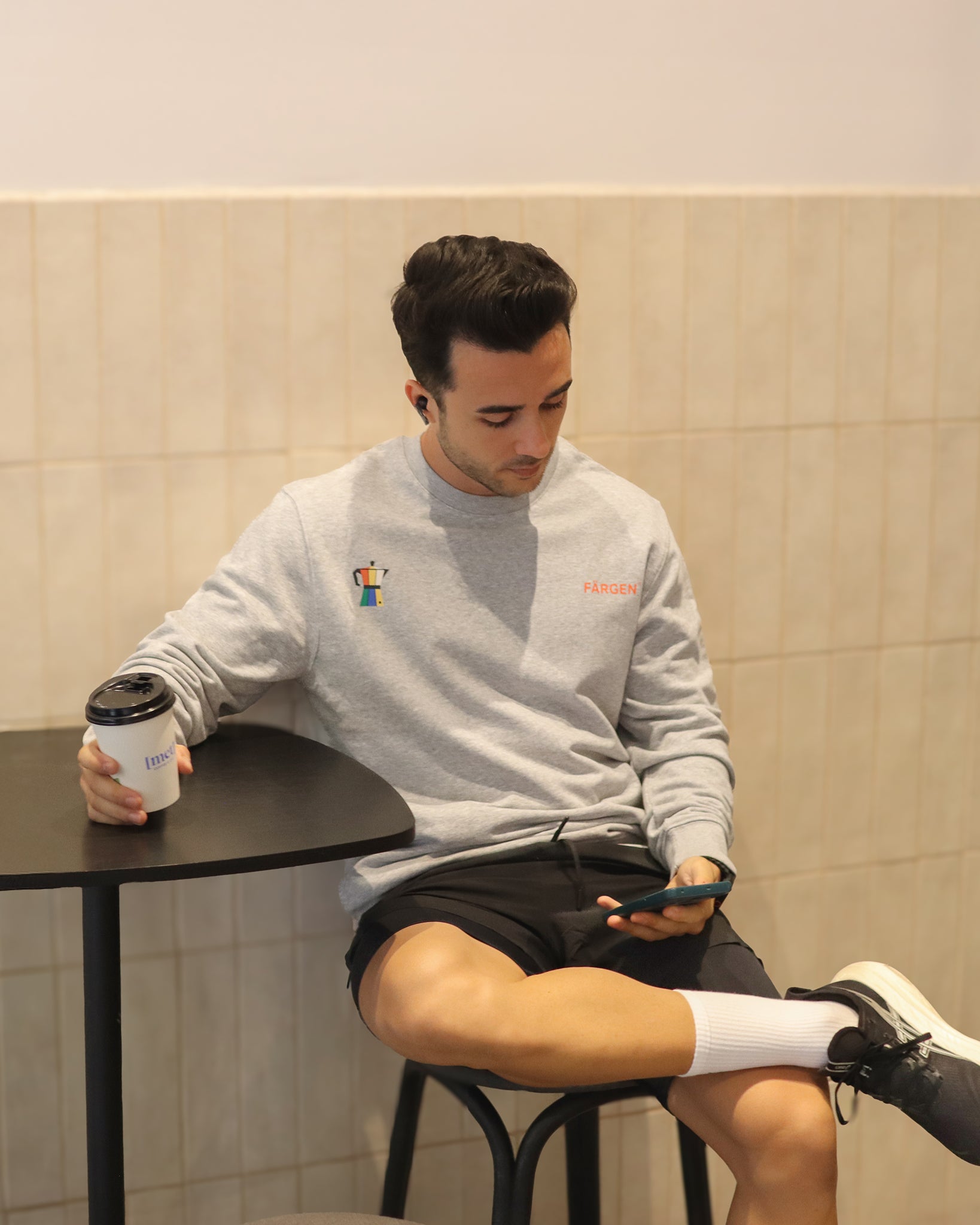 Hombre con sudadera gris Färgen Il Caffè di Casa sosteniendo un café, mostrando el diseño delantero con cafetera y logotipo Färgen.