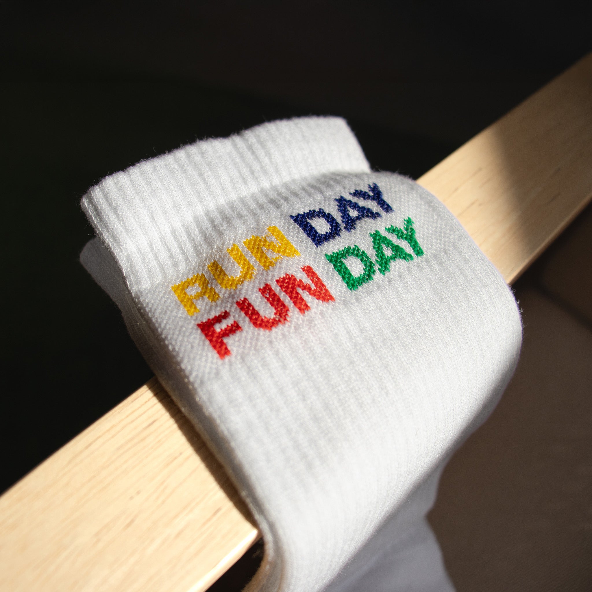 Detalle del bordado multicolor RUN DAY FUN DAY en los calcetines blancos de Färgen bajo luz natural.