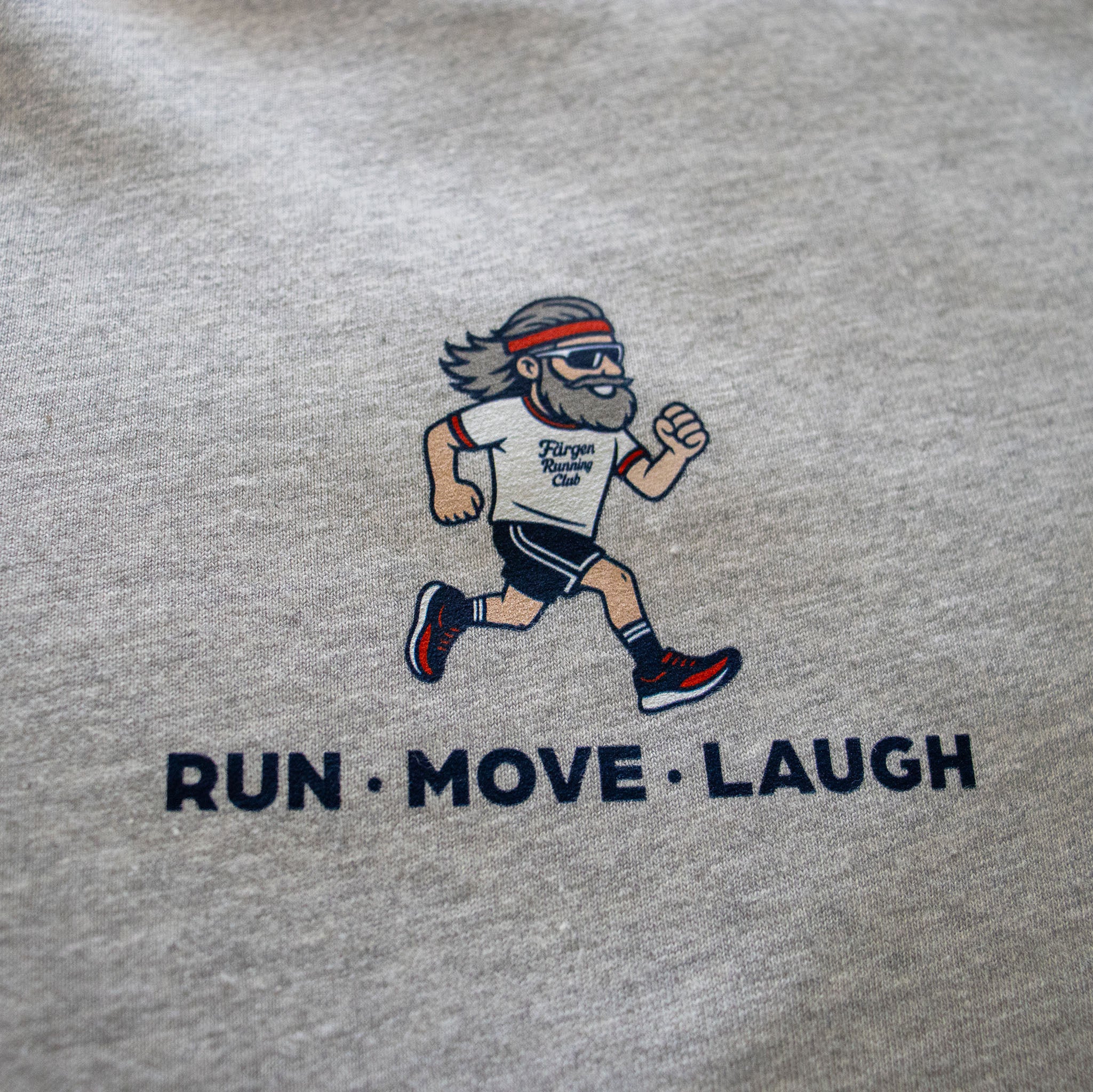 Detalle del estampado del corredor y lema RUN MOVE LAUGH en la camiseta gris Färgen Running Club.