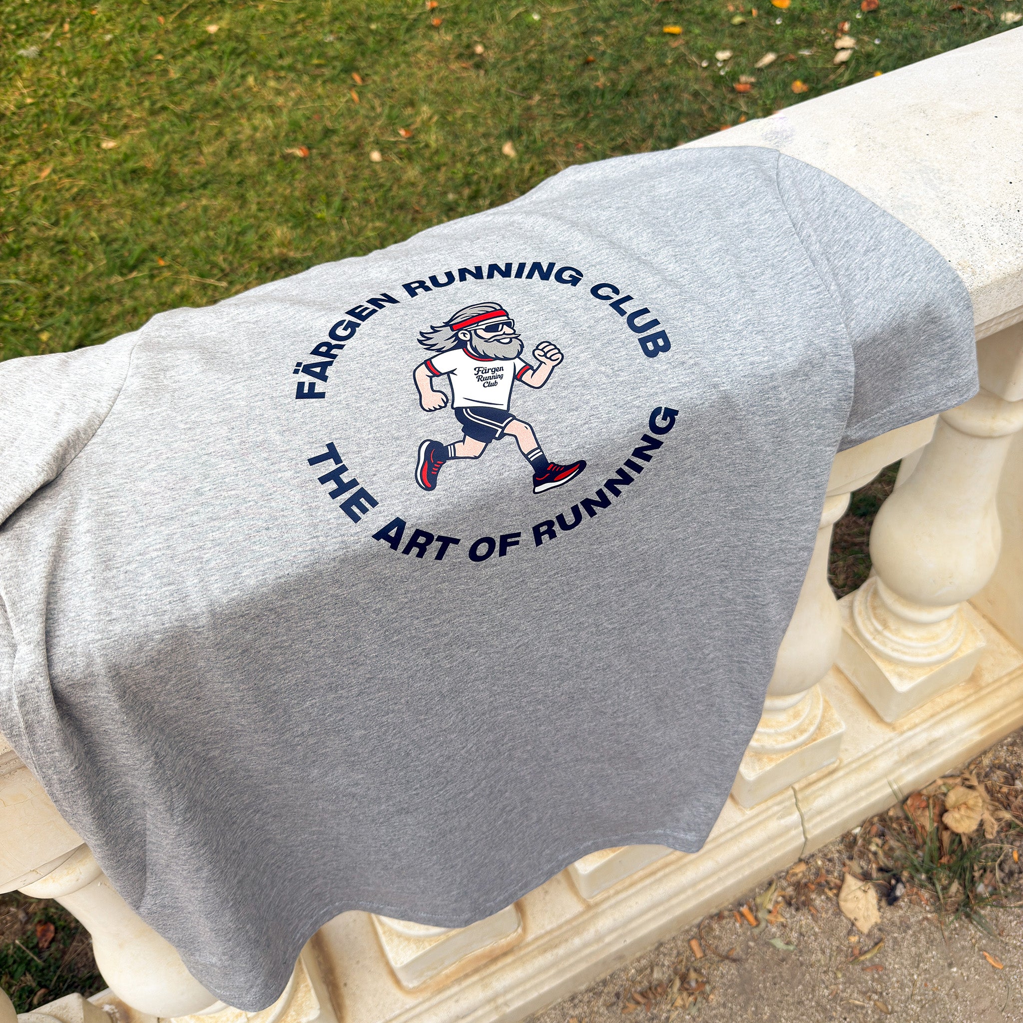 Camiseta gris Färgen Running Club doblada sobre barandilla mostrando el diseño trasero con corredor y texto The Art of Running.