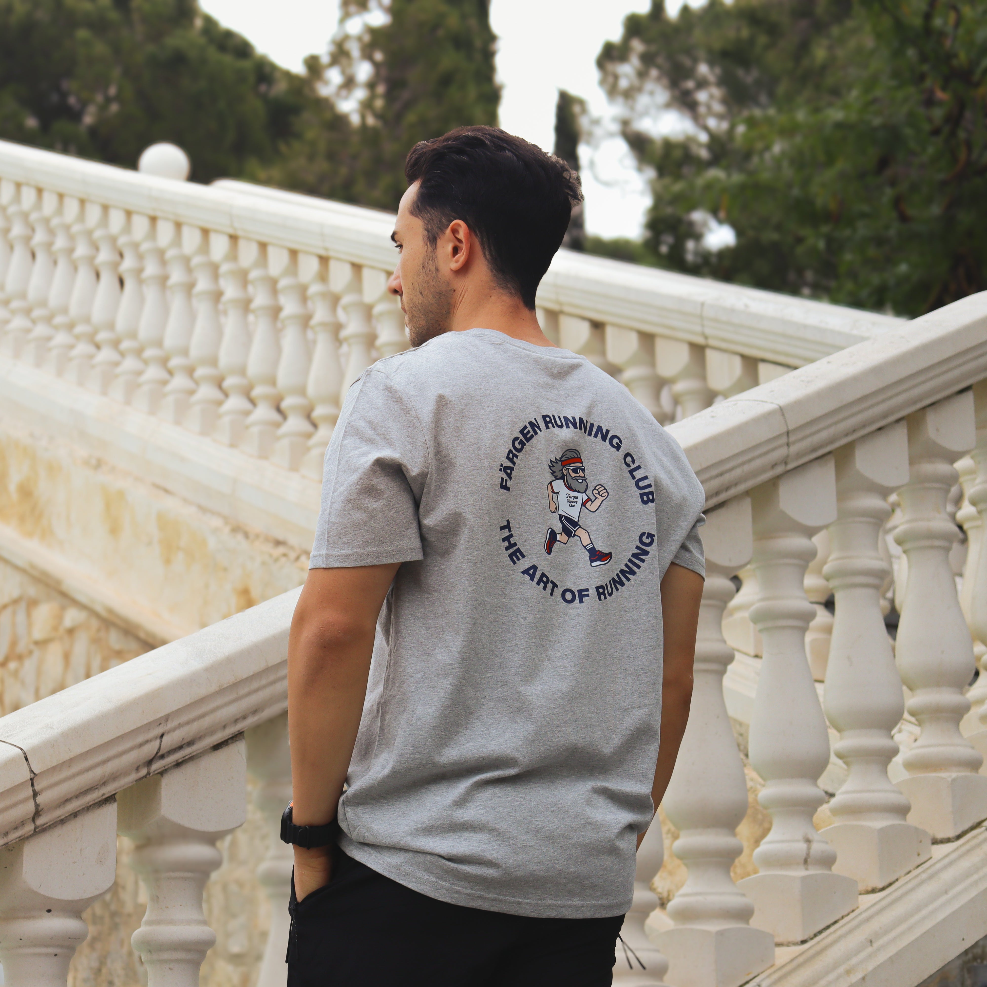 Hombre con camiseta gris Färgen Running Club mostrando el diseño trasero con corredor y texto The Art of Running.