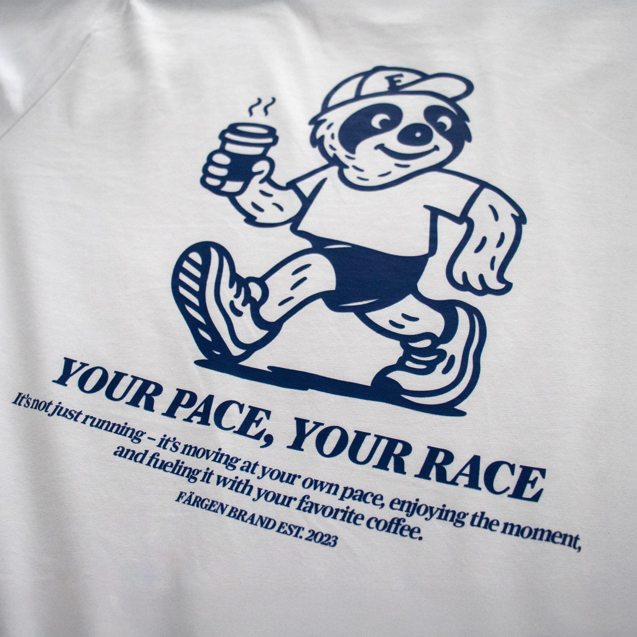 Detalle del diseño trasero de la camiseta Färgen Your Pace Your Race con perezoso corriendo y taza de café.