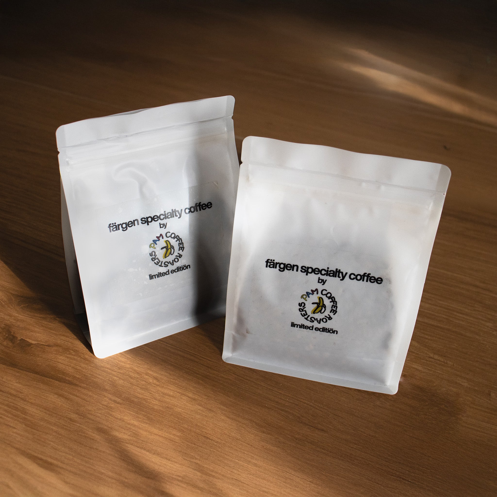 Dos bolsas de café Färgen Specialty Coffee x Pam Coffee Roasters edición limitada, colocadas sobre una superficie de madera.
