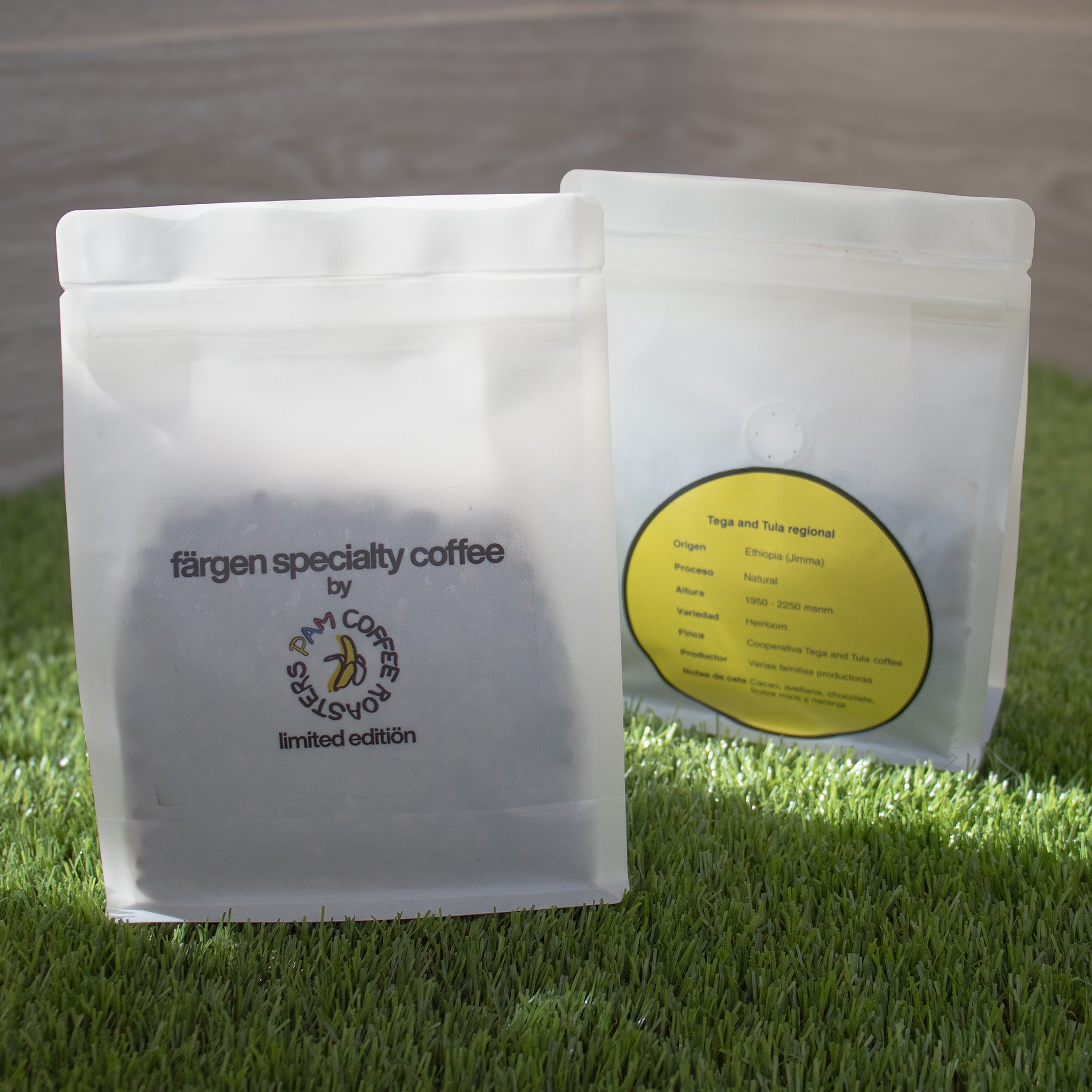 Bolsas del café Färgen Specialty Coffee x Pam Coffee Roasters sobre césped, mostrando el diseño frontal y la etiqueta de origen Etiopía Tega & Tula.