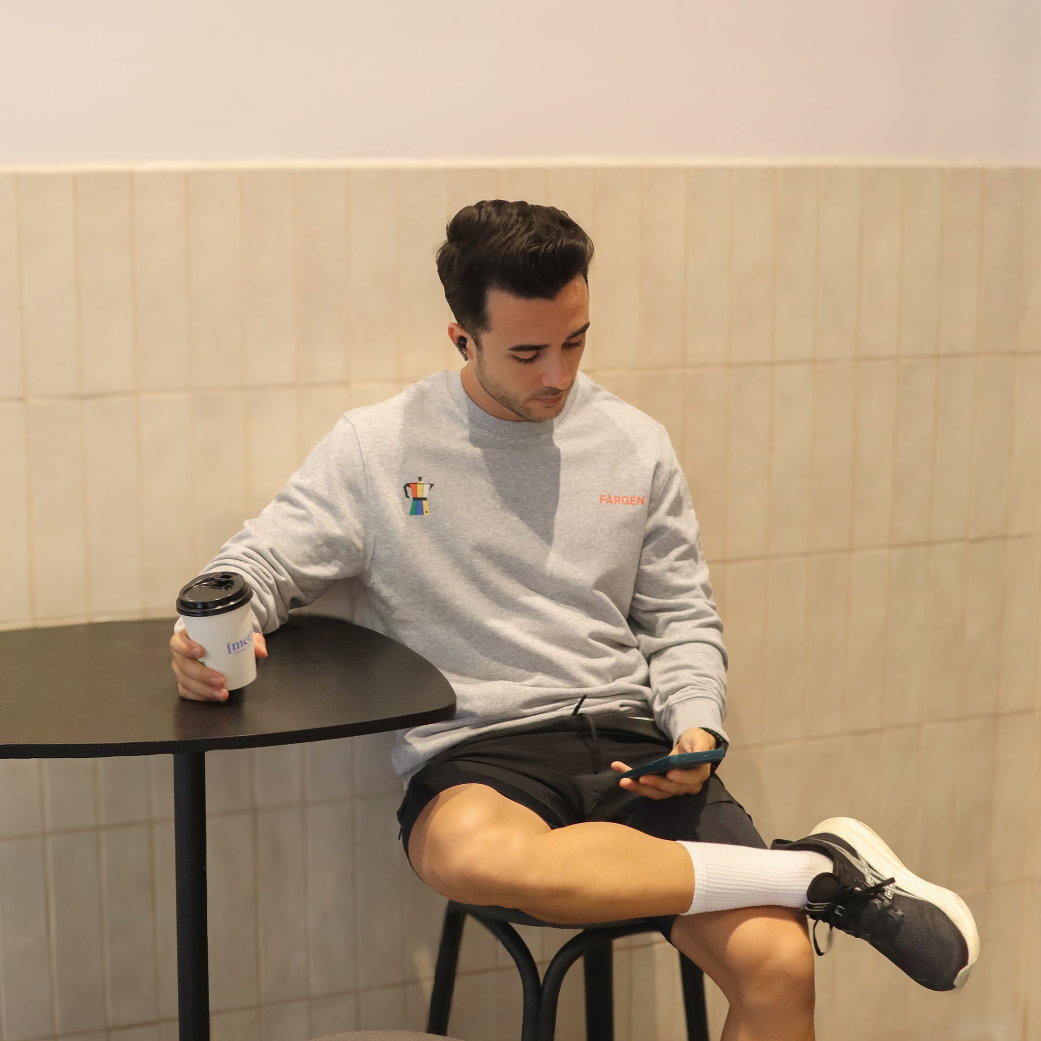 Hombre con sudadera gris Färgen Il Caffè di Casa sosteniendo un café, mostrando el diseño delantero con cafetera y logotipo Färgen.